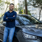 Motorista de aplicativo ao lado de carro novo em área urbana brasileira