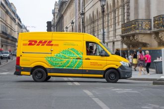 Van elétrica de entregas circulando por uma movimentada rua de Paris em um dia ensolarado.