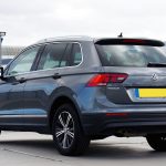 Volkswagen Tiguan cinza visto de traseira, estacionado em uma área urbana.