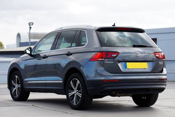 Volkswagen Tiguan cinza visto de traseira, estacionado em uma área urbana.