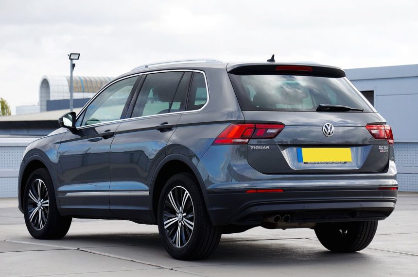 Volkswagen Tiguan cinza visto de traseira, estacionado em uma área urbana.