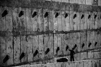 Dois trabalhadores pintam uma grande parede de concreto em uma obra em Londrina, no Paraná.